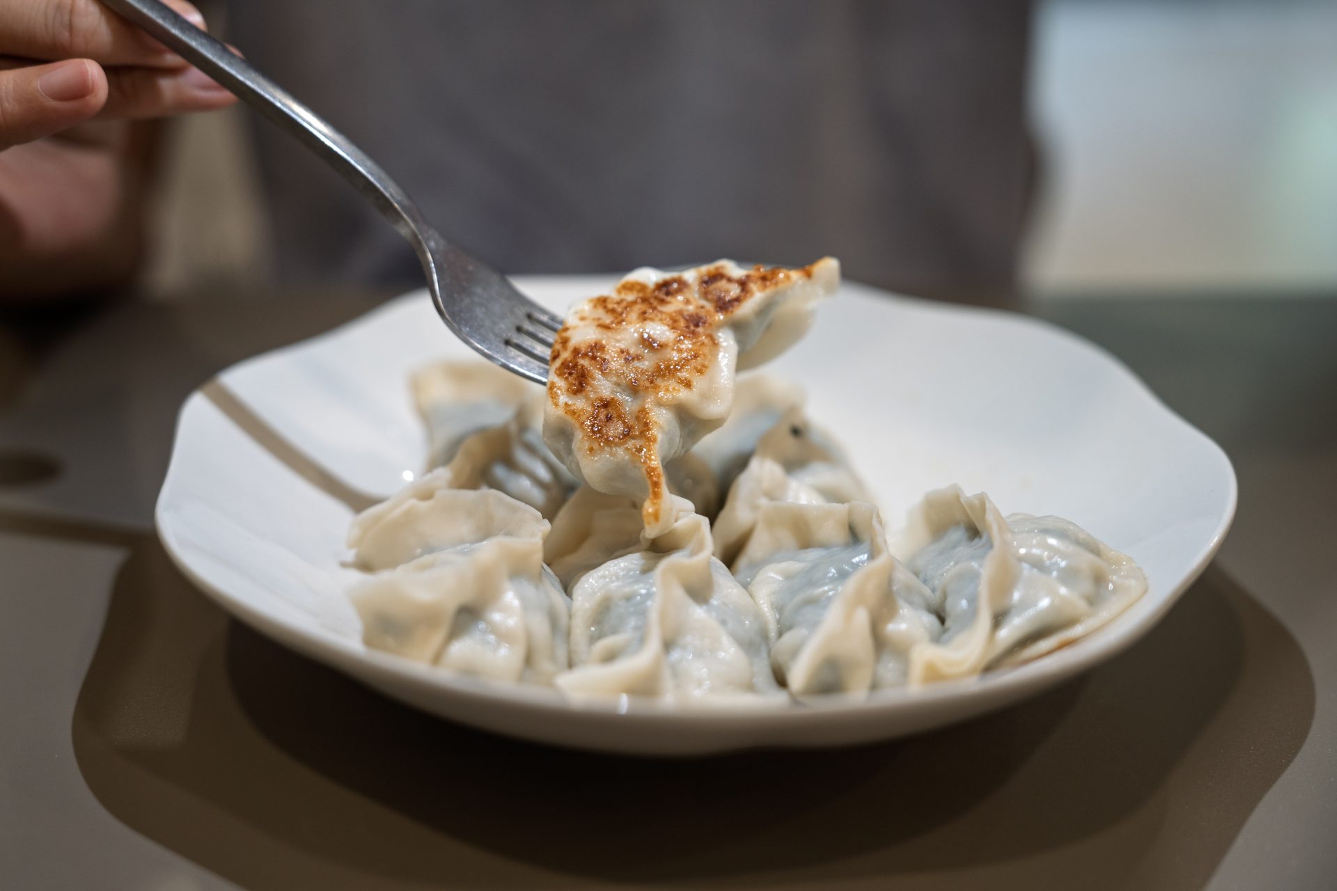 Person Eating Pan-Fried Dumpling on White Plate Steamed and pan fried gyoza until crispy. Ready to enjoy